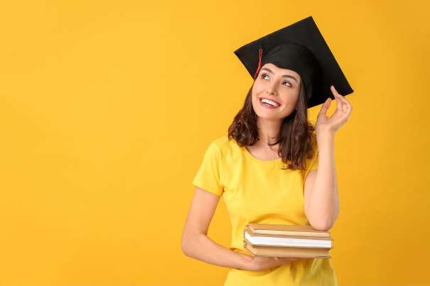 A young woman in a graduation cap and gown holding books, symbolizing academic achievement and success.